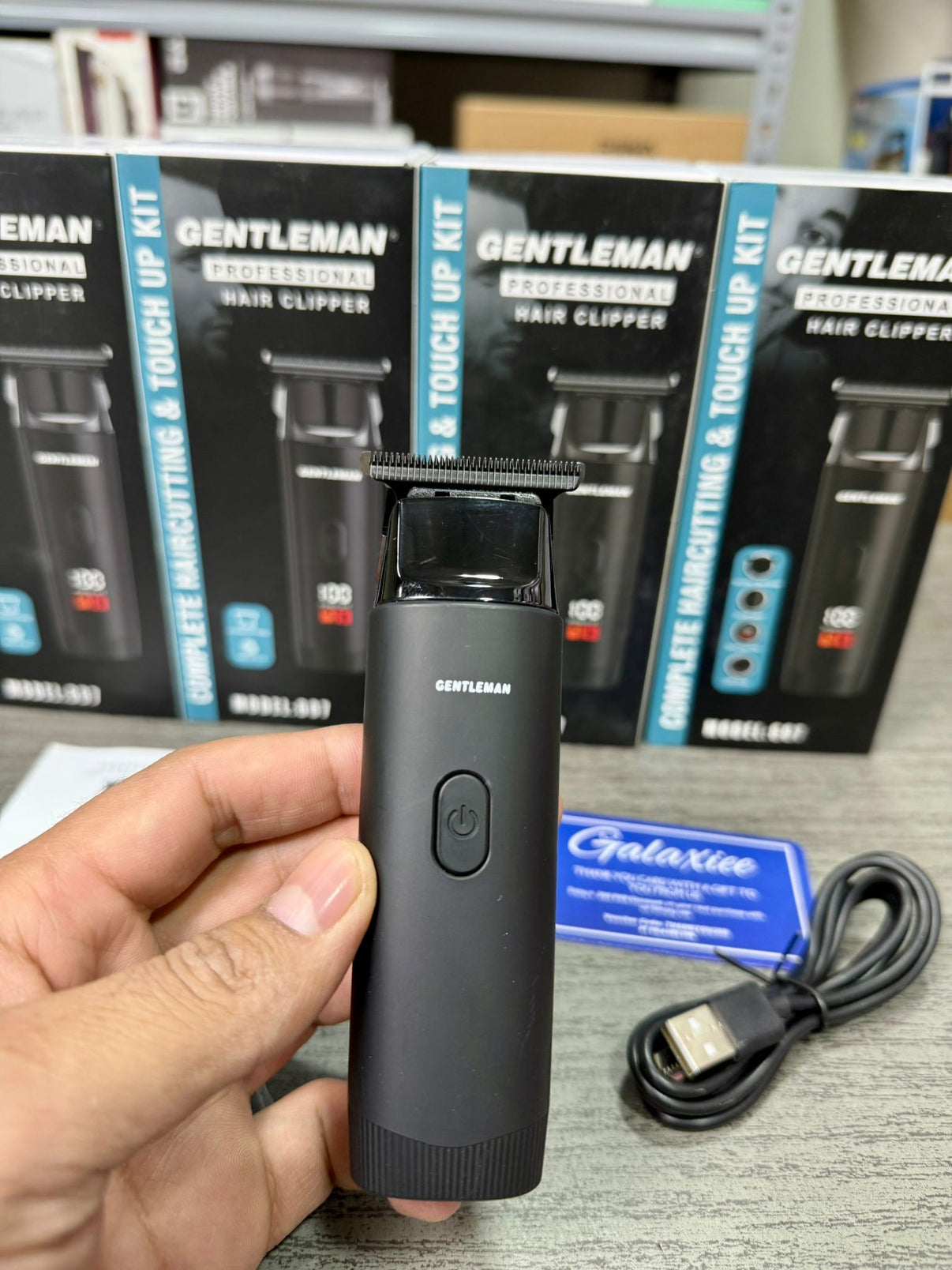 Gentleman professional hair clipper packaging held by a hand with additional products in the background.
